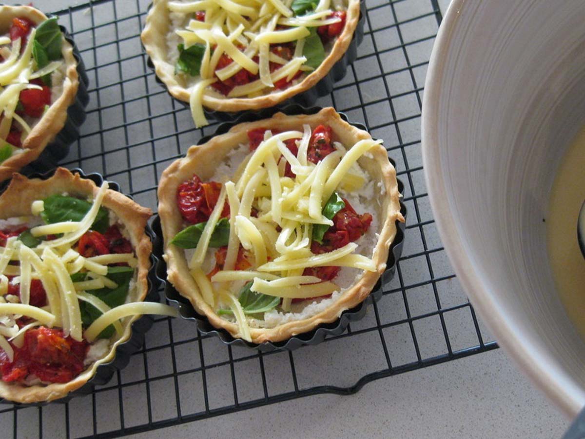 A vibrant vegetarian quiche baked with sun-dried tomatoes, fresh basil leaves, and crumbled feta cheese.