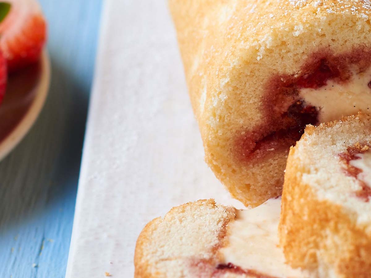 A classic golden sponge swiss roll cake rolled tightly with sweet strawberry jam filling.