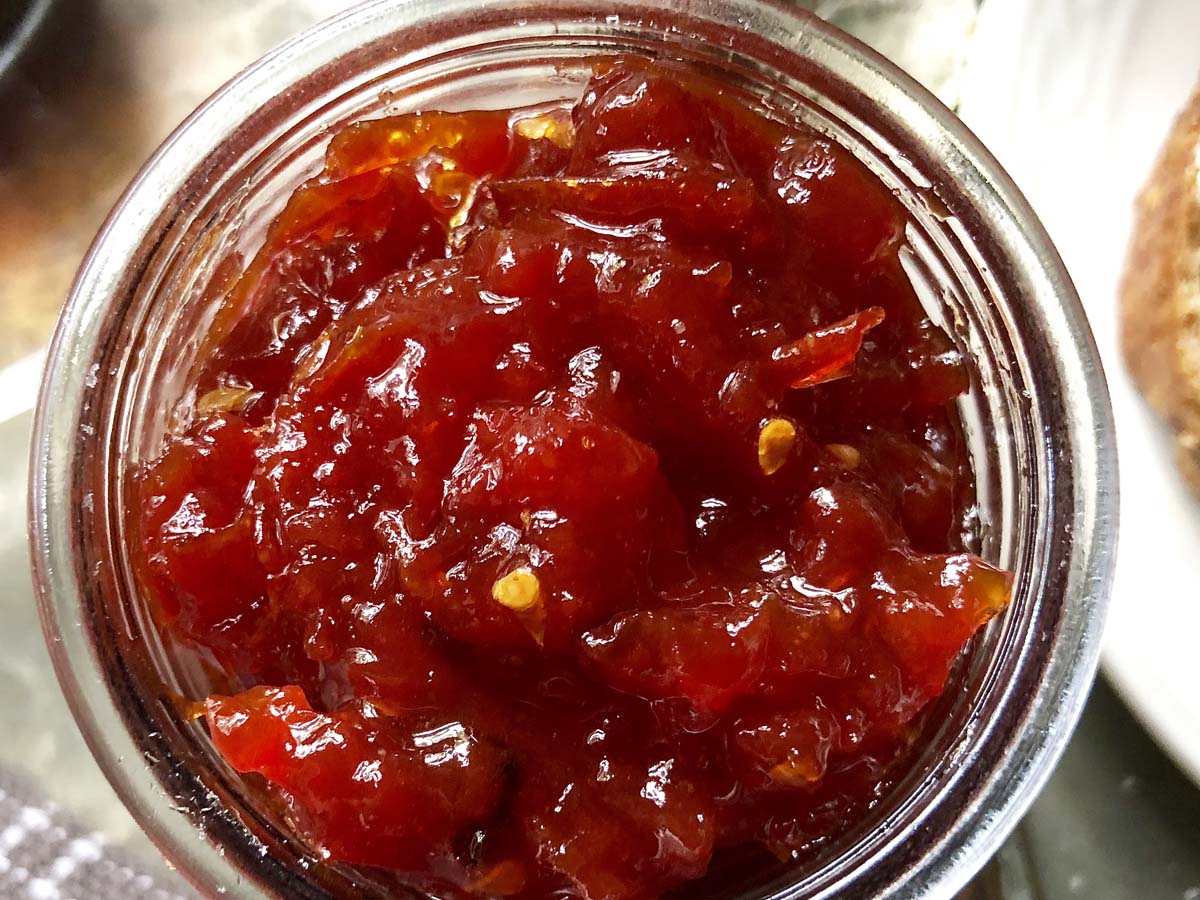 Vibrant red sweet tomato and chili jam relish in a clear serving container.