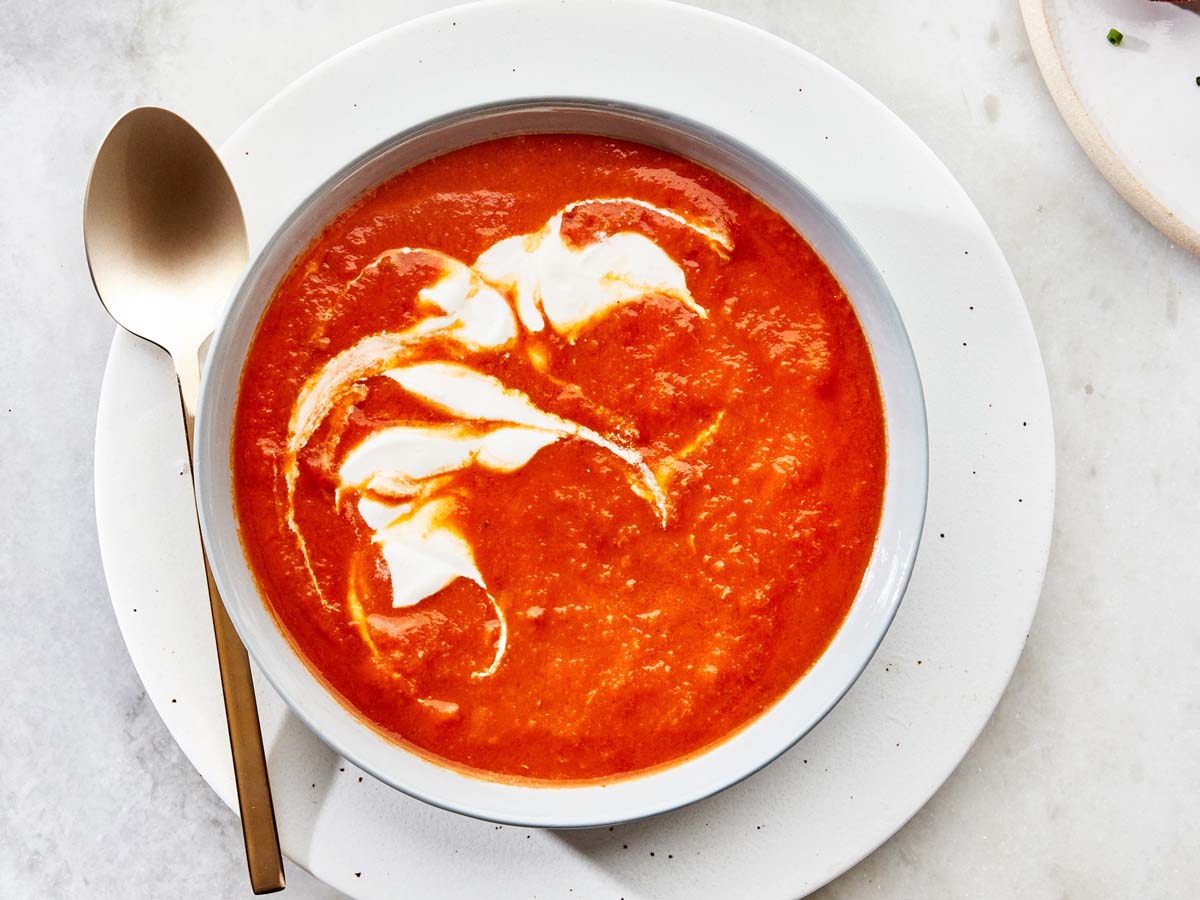 A classic, vibrant smooth tomato soup served hot in a deep soup bowl.