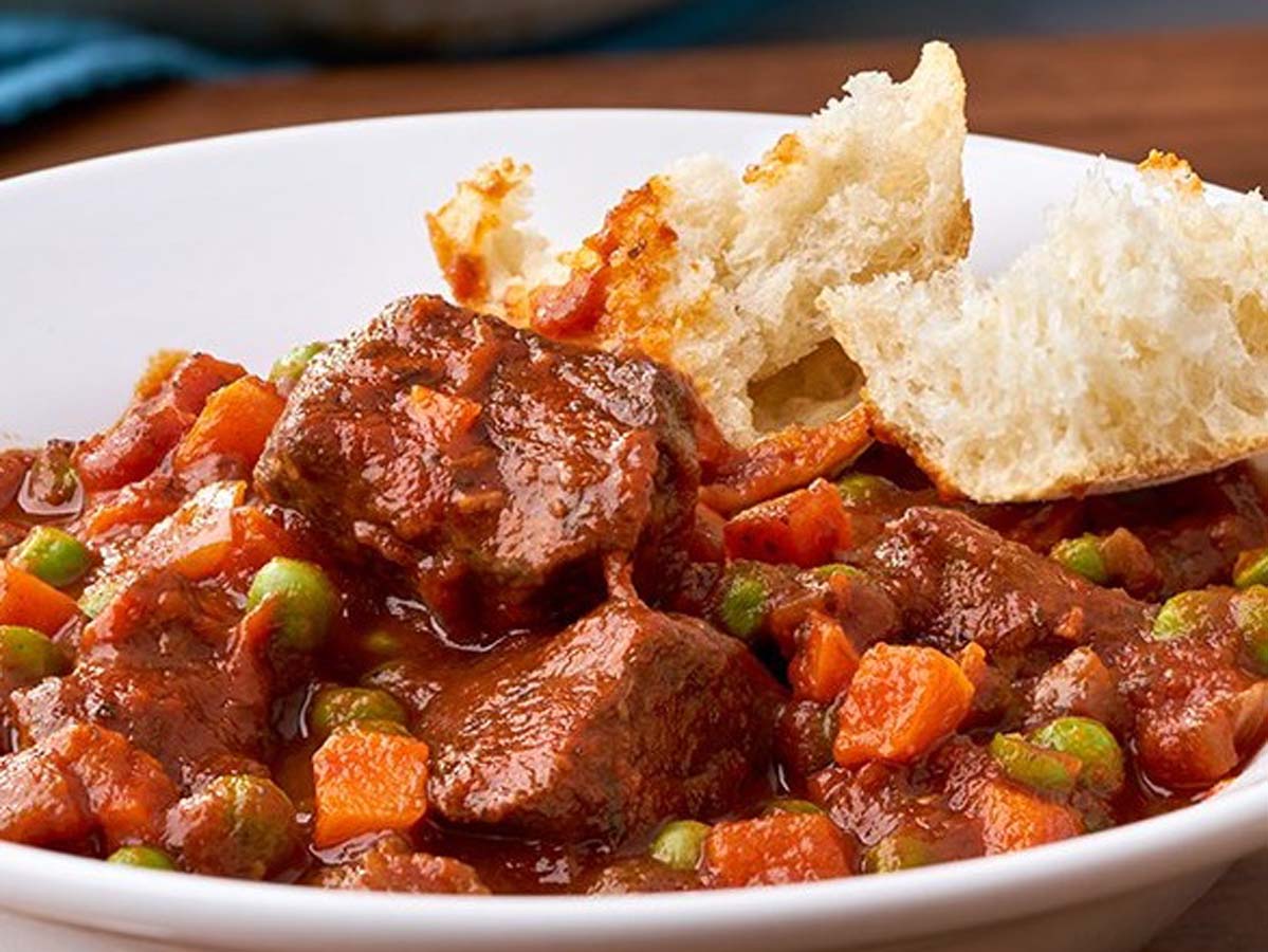A rich and thick homemade tomato stew simmering with fresh herbs in a pot.
