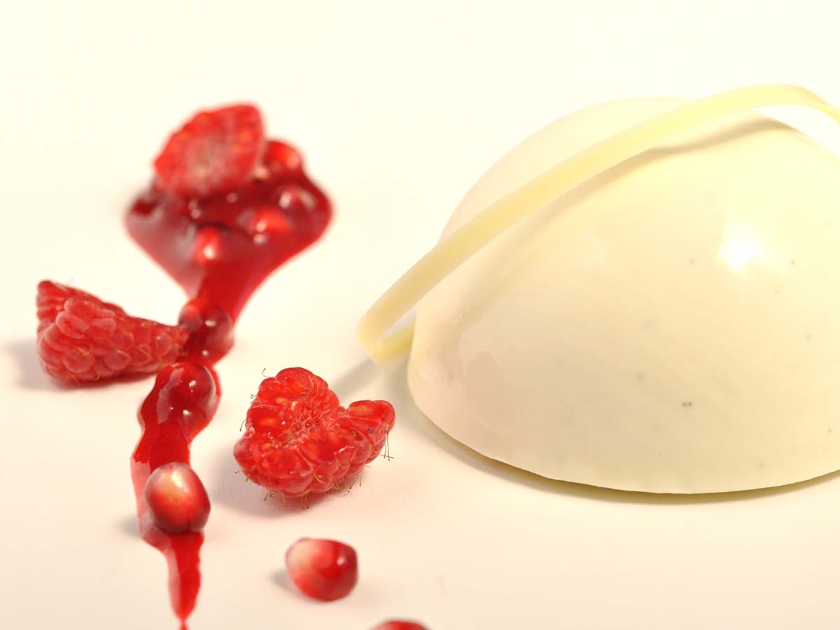 A molded vanilla Bavarian cream dessert wobbling gently next to fresh fruit berries.