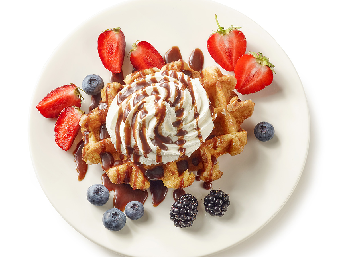 Crispy hot waffles topped with fresh sliced sweet strawberries and a mound of whipped cream.